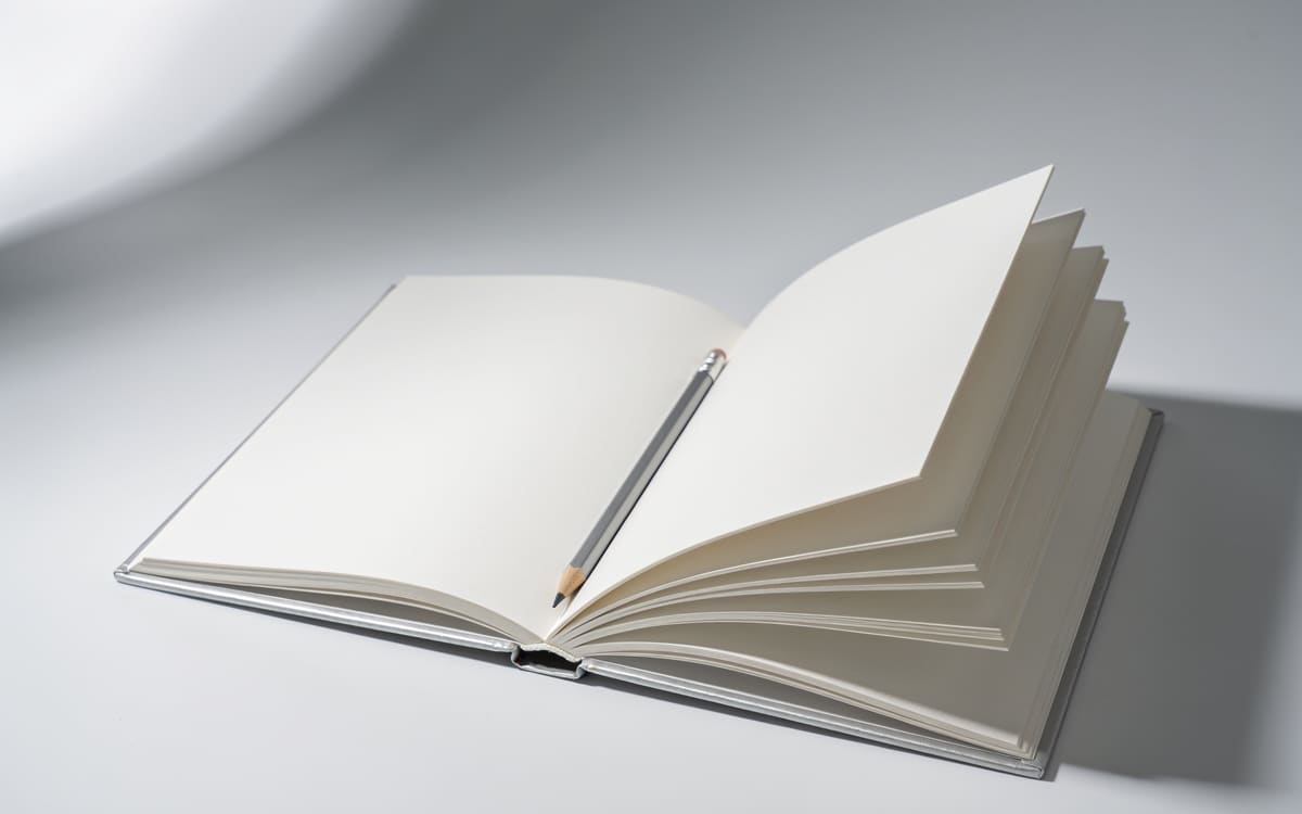 An open book with blank pages and a pencil resting across them on a light grey studio background