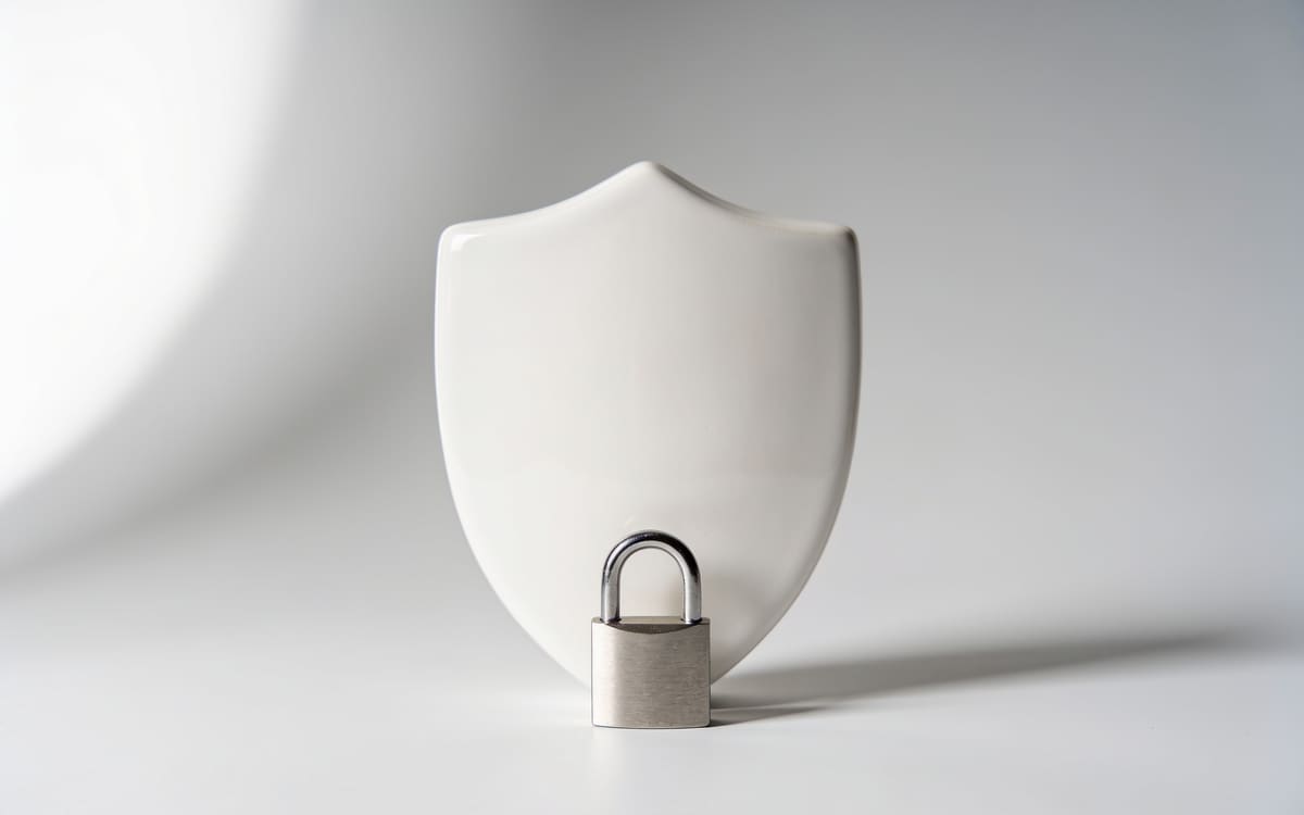 A white ceramic shield with a small silver padlock in front, on a light grey studio background