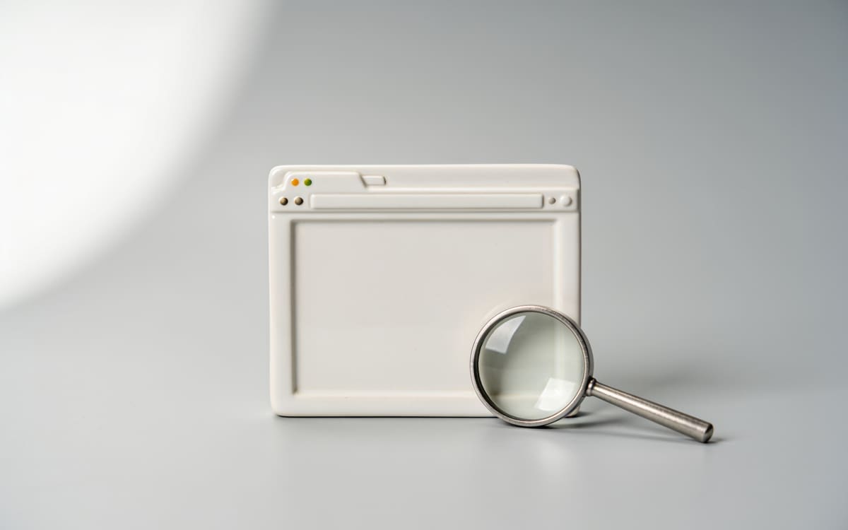 A white ceramic browser window with a blank screen and a silver magnifying glass, on a light grey studio background