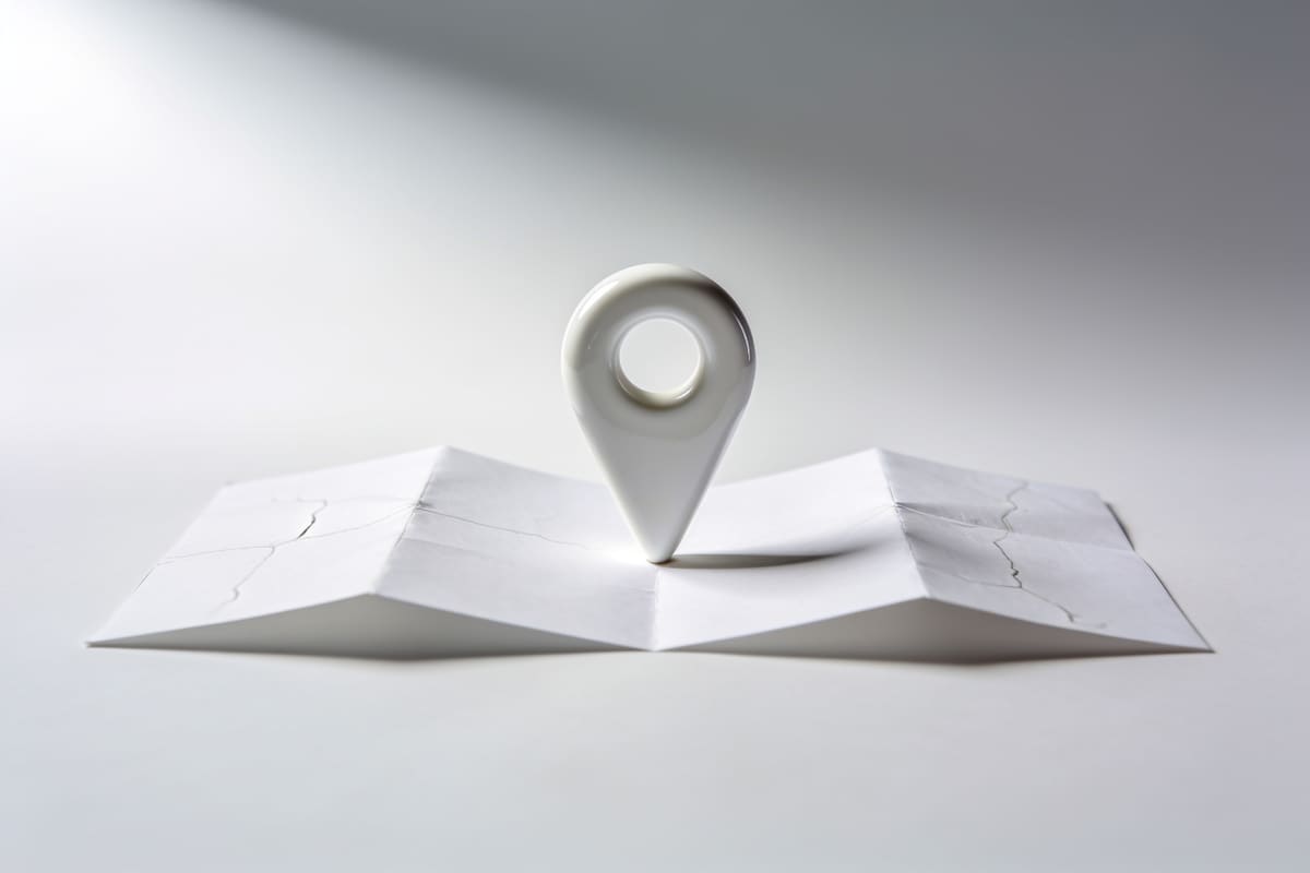 A white ceramic map pin standing on a folded blank paper map on a light grey studio background